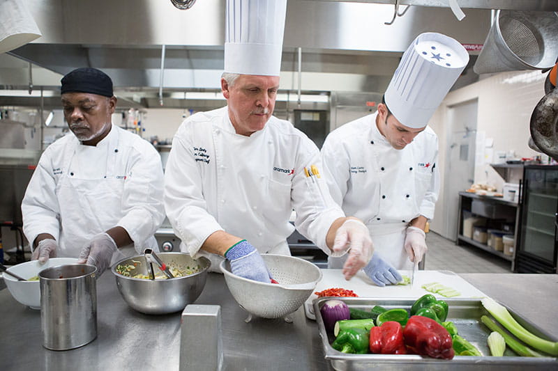Racially diverse group of chefs prepping food in professional kitchen.